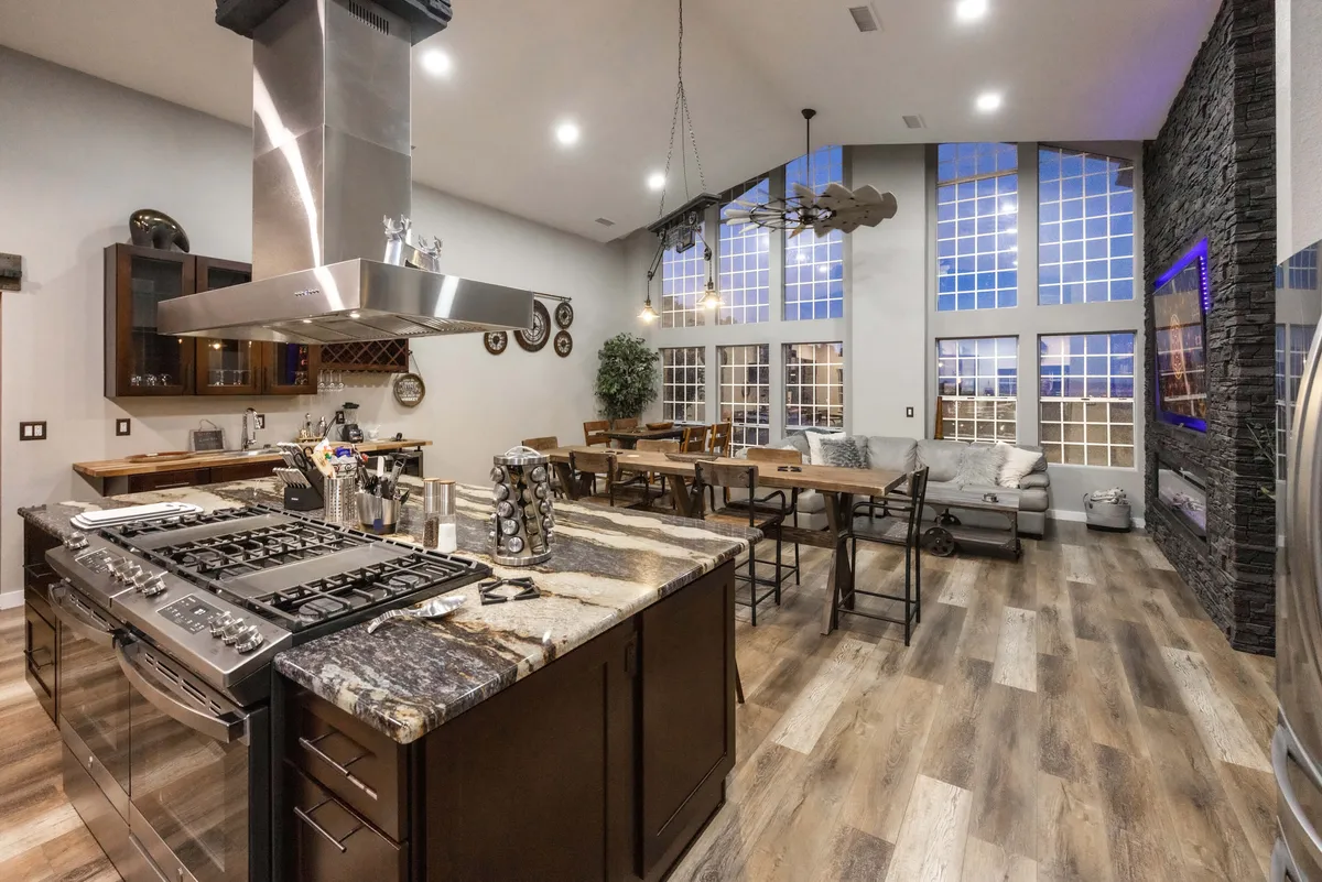 A contemporary kitchen and dining space with a large island ideal for group food prep, stainless steel appliances, a cozy dining table, and expansive windows that bathe the space in natural light, offering scenic sunset views to enhance meal times.