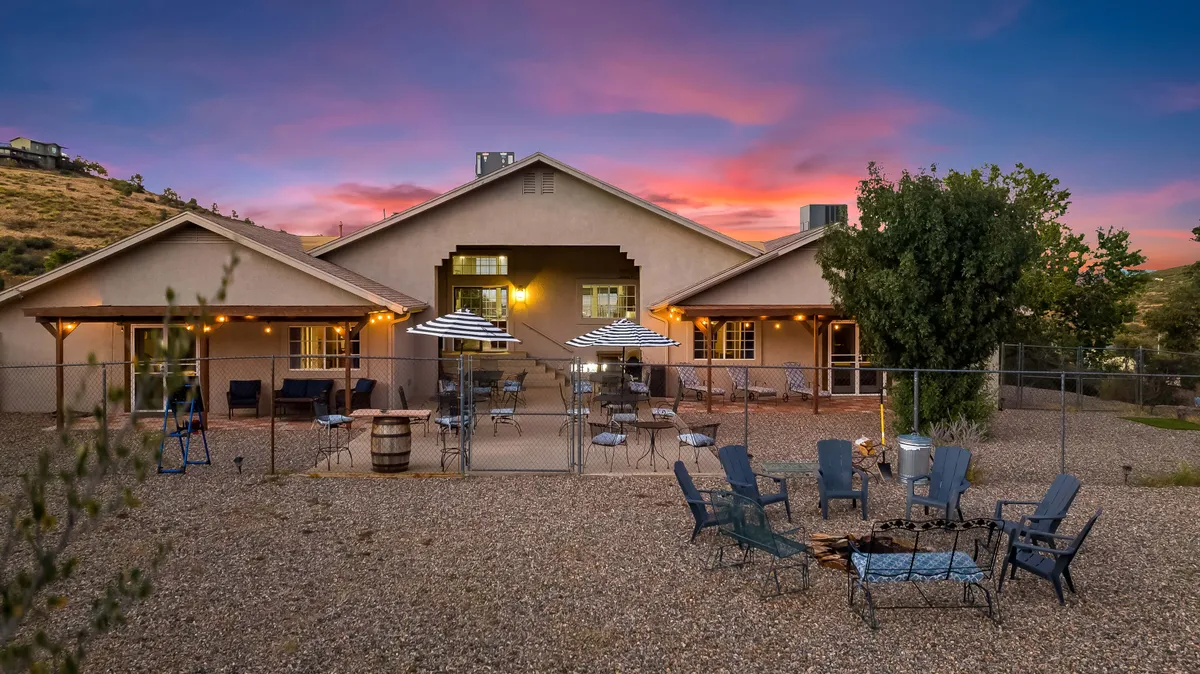 A welcoming patio seating area with a fire pit, outdoor umbrellas, and landscaped surroundings, set against a hillside backdrop. The scene is designed for social gatherings, relaxation, and enjoying the outdoors well into the evening.