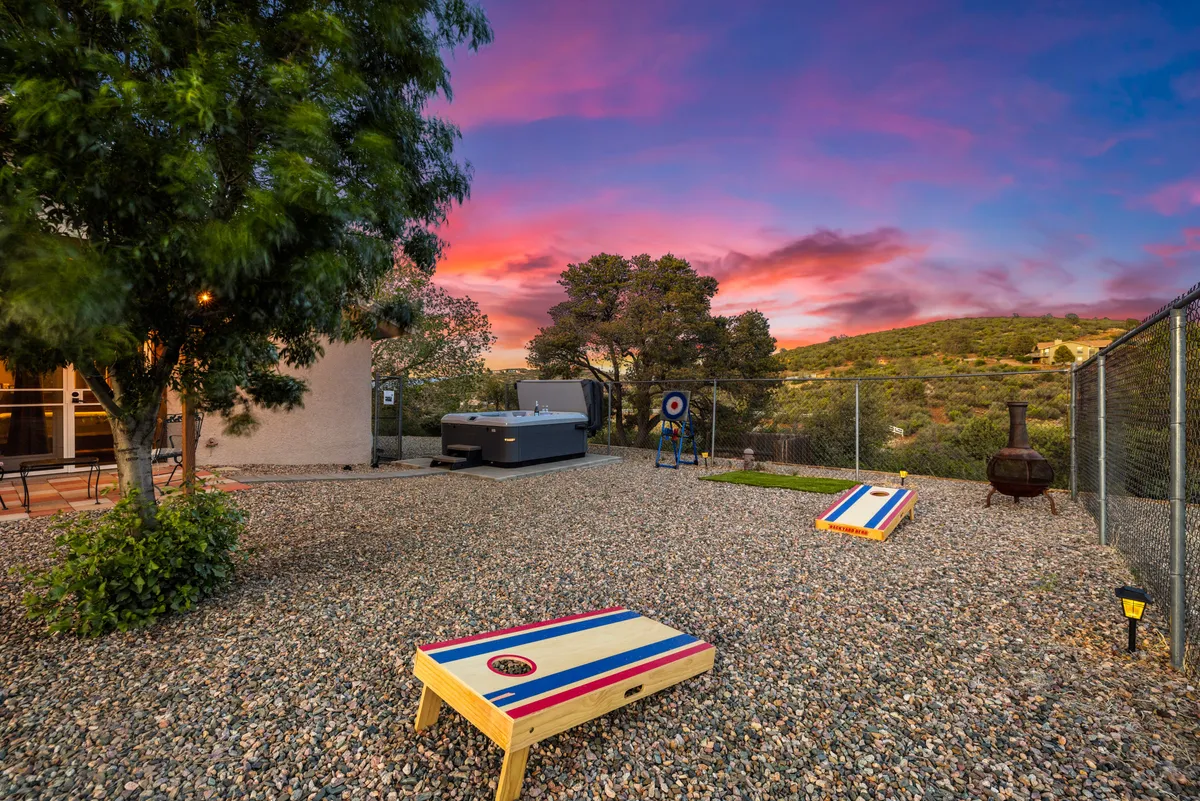 An outdoor scene featuring cornhole boards set on the lawn, a hot tub ready for relaxation, a fire pit with seating for evening gatherings, and a scenic landscape backdrop. The area is arranged to encourage both active play and laid-back moments under the sky.