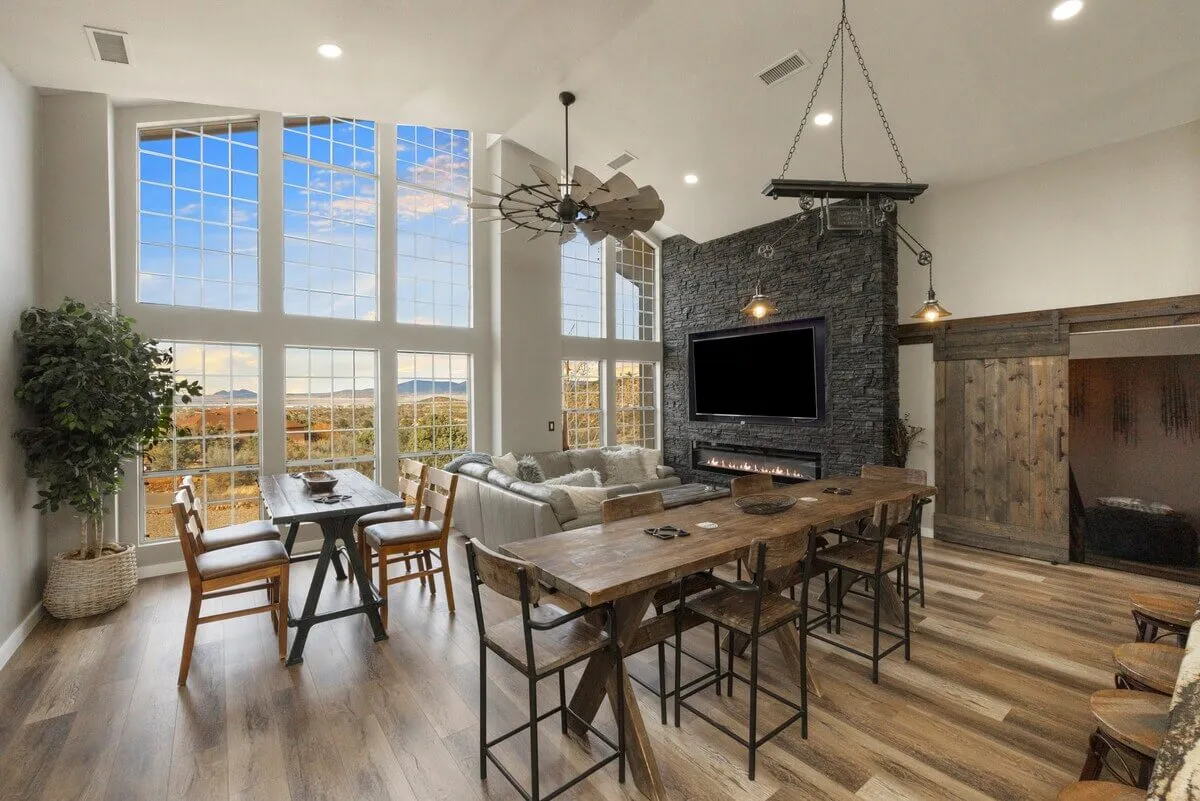 A warm, welcoming great room with a long dining table, plush sofa, a stone accent wall with fireplace, and large windows overlooking the mountains. The space is ideal for group dinners, game nights, or relaxing by the fire, with décor that is both rustic and refined.