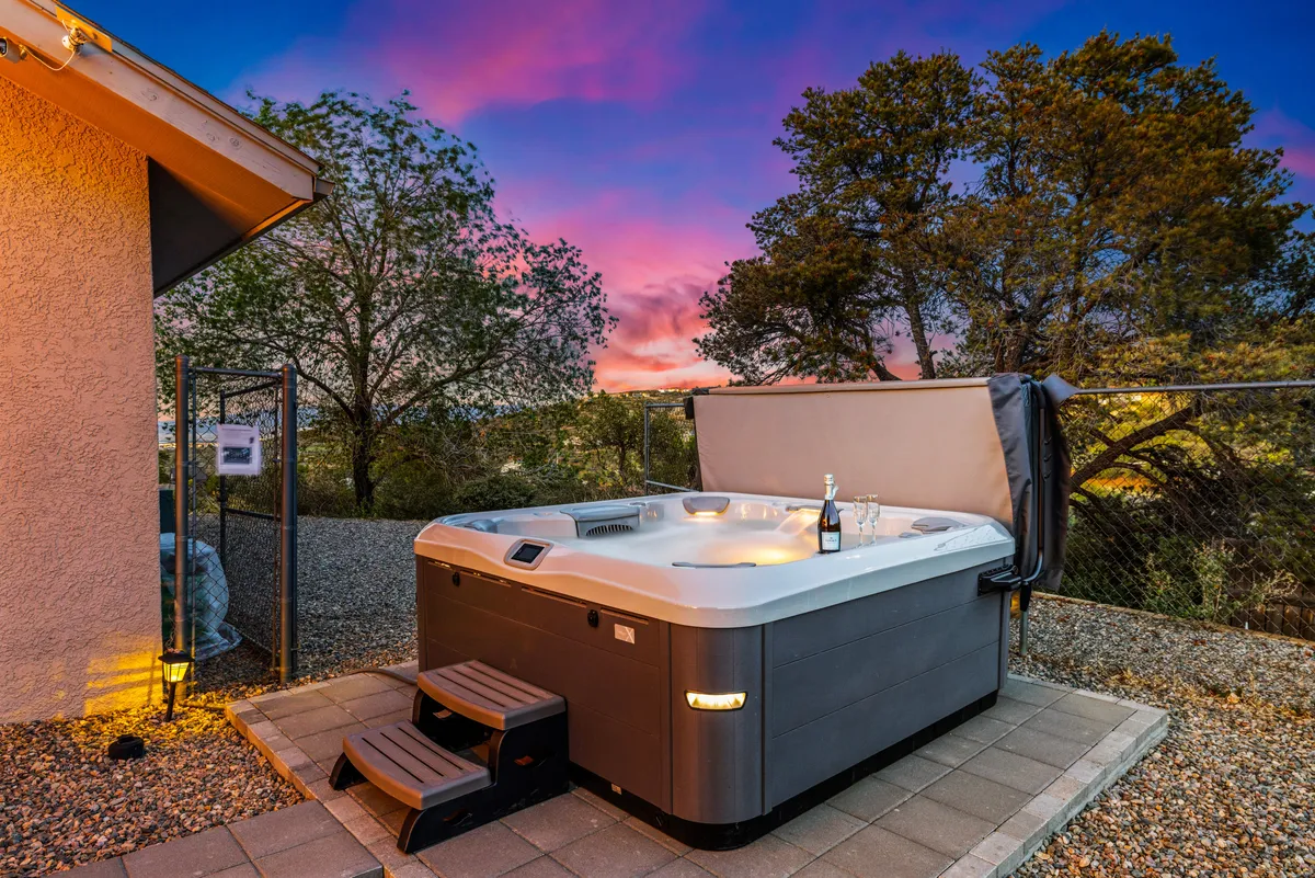 A tranquil exterior image featuring a hot tub on the patio, a bottle of champagne, and a breathtaking sunset sky. The hot tub overlooks the natural surroundings, offering a space for relaxation, celebration, and stargazing with colleagues or friends after a day of workshops.