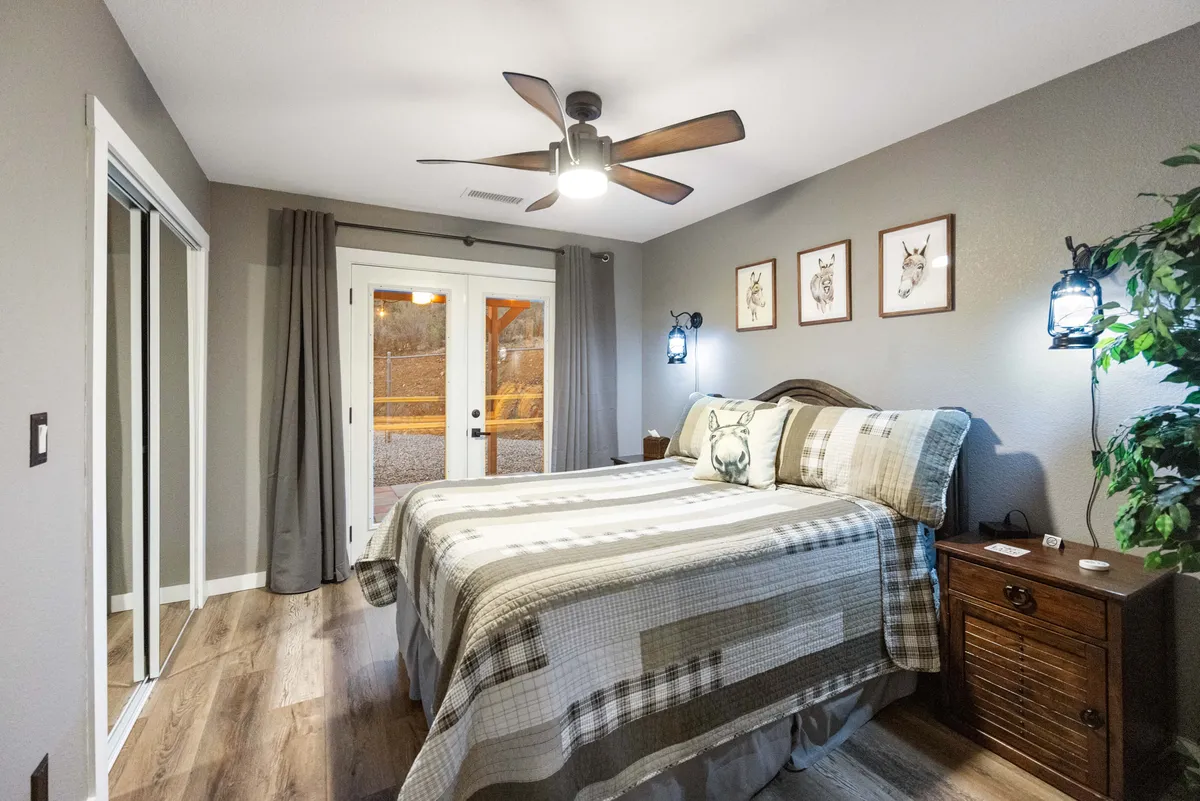 A tranquil bedroom featuring a bed with a patterned quilt, double doors leading outside, and artwork on the wall. The room is filled with natural light, creating a restful, inviting atmosphere that encourages relaxation and comfort.