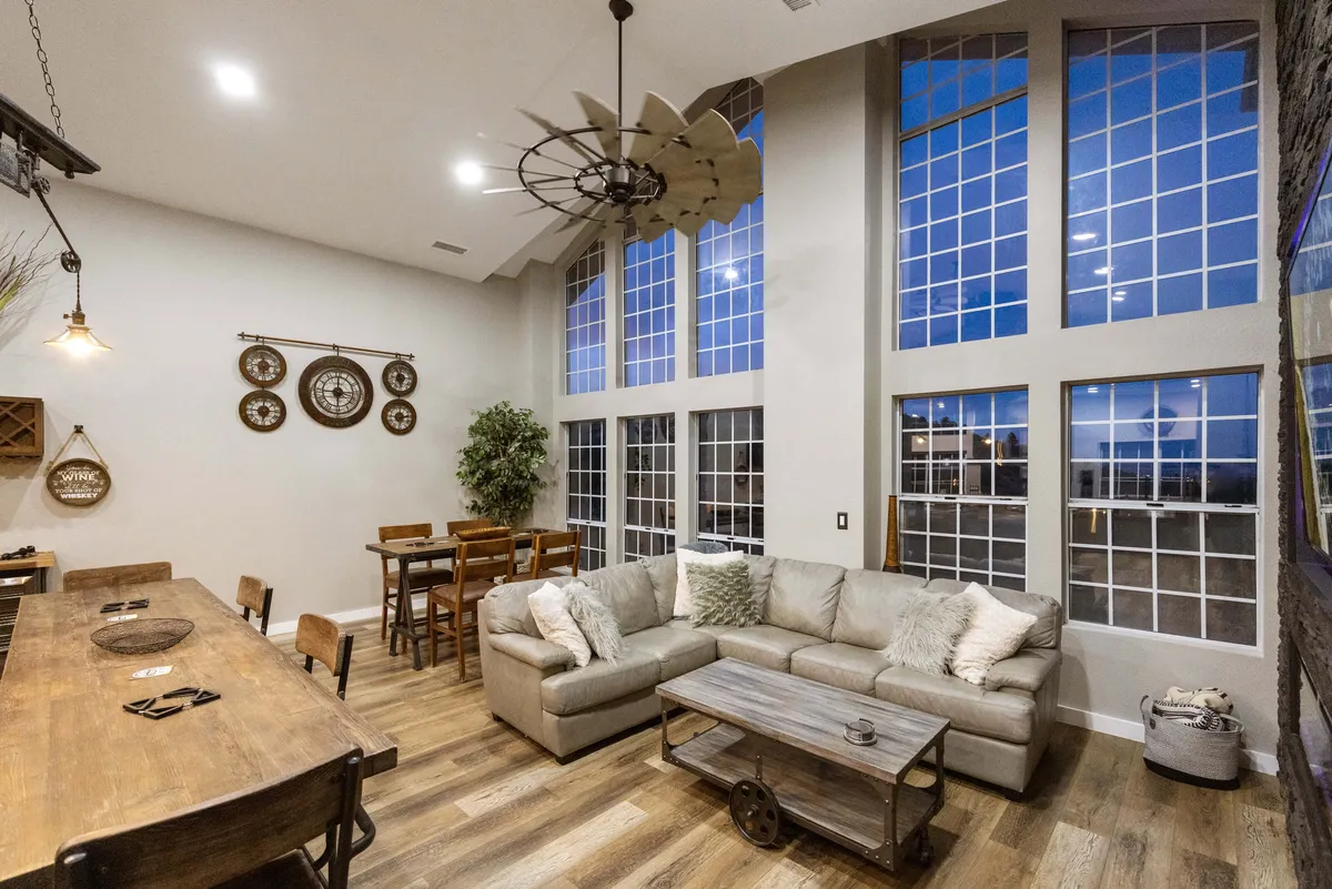 An open-plan social space with a seating area, a dining table, large windows offering sunset views, and decorative wall pieces. The area is filled with natural light and designed for group gatherings, featuring both comfort and style.